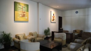 A modern living room with striped sofas, a coffee table, and two large abstract paintings. - Hotel Green Wattana Sentul (Citaringgul)