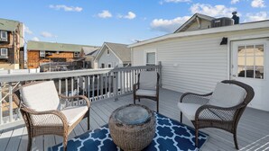 A covered deck with wicker chairs and a round table, overlooking a residential area. - 2 BR Ocean Block Home (Seaside Park)