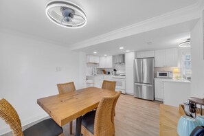 Eine moderne Küche mit weißen Schränken, Edelstahlgeräten und einem Esstisch aus Holz mit Korbstühlen.
