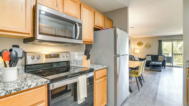 A modern kitchen with granite countertops, stainless steel appliances, wooden cabinets, and a dining area with a table and chairs. - 2 Mi to Branson Strip: Family Condo w/ Balcony! (Branson)