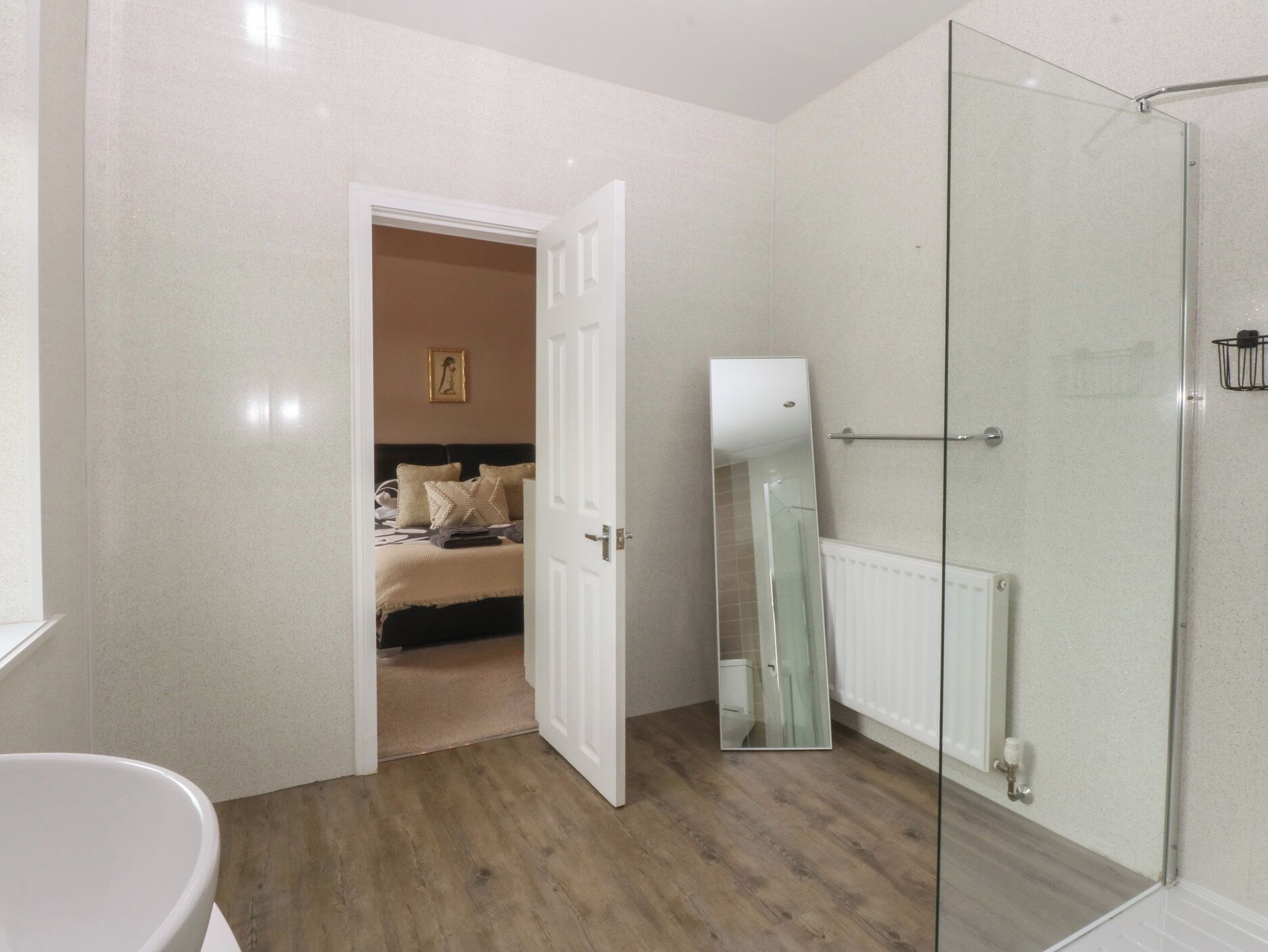 A modern bathroom with a shower, a large mirror, and a wooden floor.
