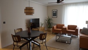 A modern living room with a round dining table, two sofas, a coffee table, and a TV. - Serendipity (Zaragoza)