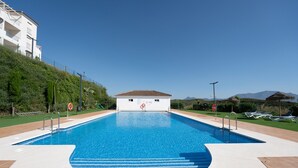 A swimming pool with clear blue water, surrounded by a tiled deck, and a lifeguard stand. - Small Oasis Manilva - Cozy Apartment (Manilva)