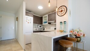 A modern kitchen with a marble island, wooden cabinets, and a clock on the wall. - Small Oasis Manilva - Cozy Apartment (Manilva)