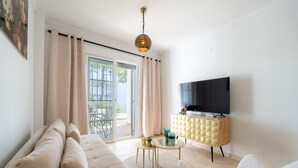 A modern living room with a sofa, armchair, and a television on a wooden cabinet. - Small Oasis Manilva - Cozy Apartment (Manilva)