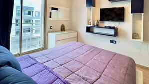 Une chambre avec un grand lit, un téléviseur fixé au mur et une fenêtre avec des rideaux.