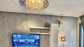 Un salon moderne avec un téléviseur à écran plat fixé au mur, un meuble de rangement blanc, une lampe sur pied et une plante en pot posée sur une table basse.