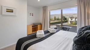 Habitación de hotel con un ventanal grande, una cama con cubrecama a rayas blanco y negro, una mesita de noche de madera y vistas a un paisaje montañoso.