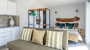 A modern bedroom with a large bed, a sofa with striped pillows, a wooden headboard, and a kitchen area with patterned tiles. - Villa's Pomar do Moinho - 5min de Óbidos (Obidos)