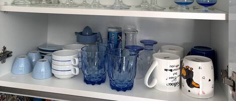 A kitchen shelf with various glassware, including wine glasses, tumblers, and a teapot.