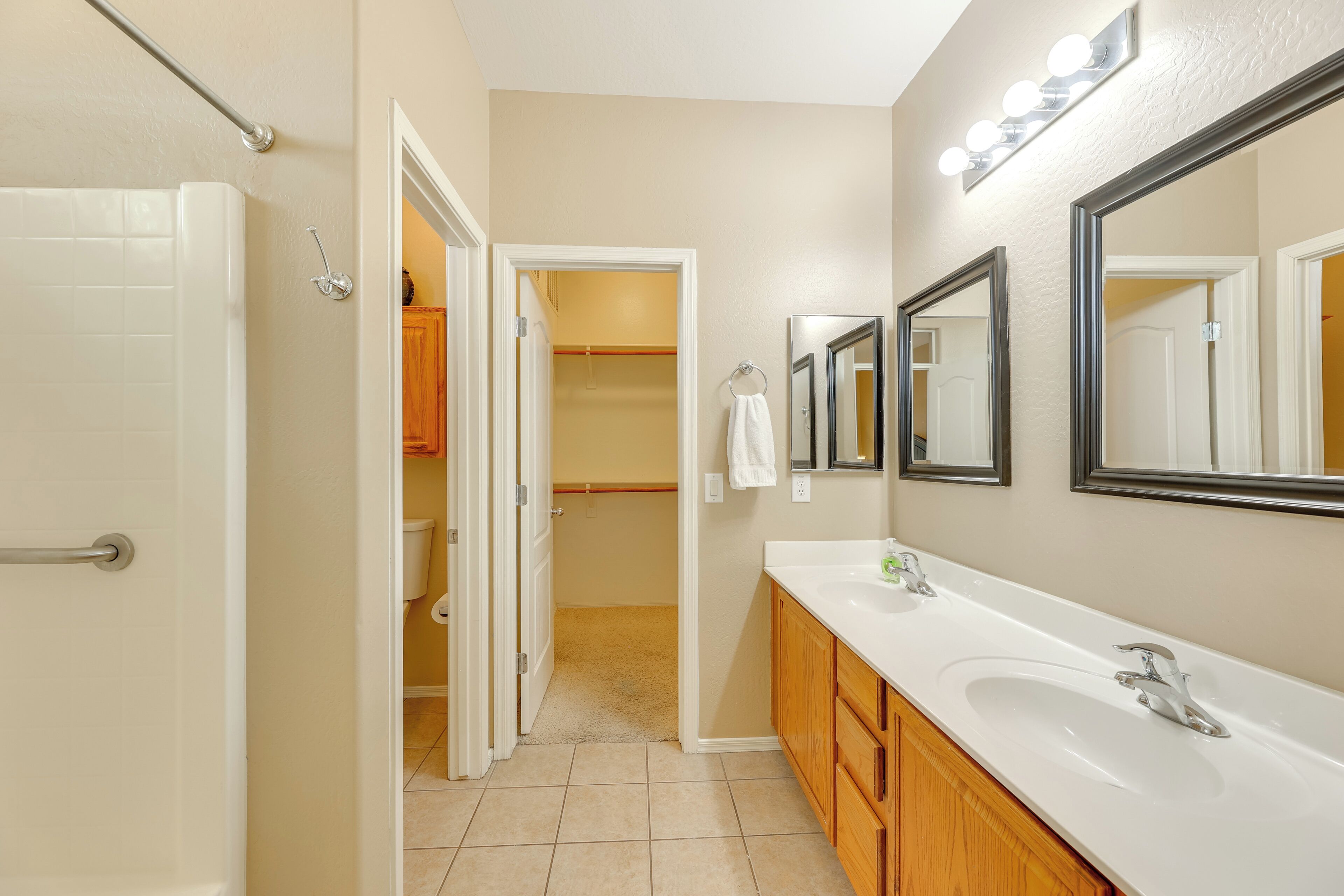 A bathroom with a white sink, wooden cabinets, a large mirror, and a walk-in closet.
