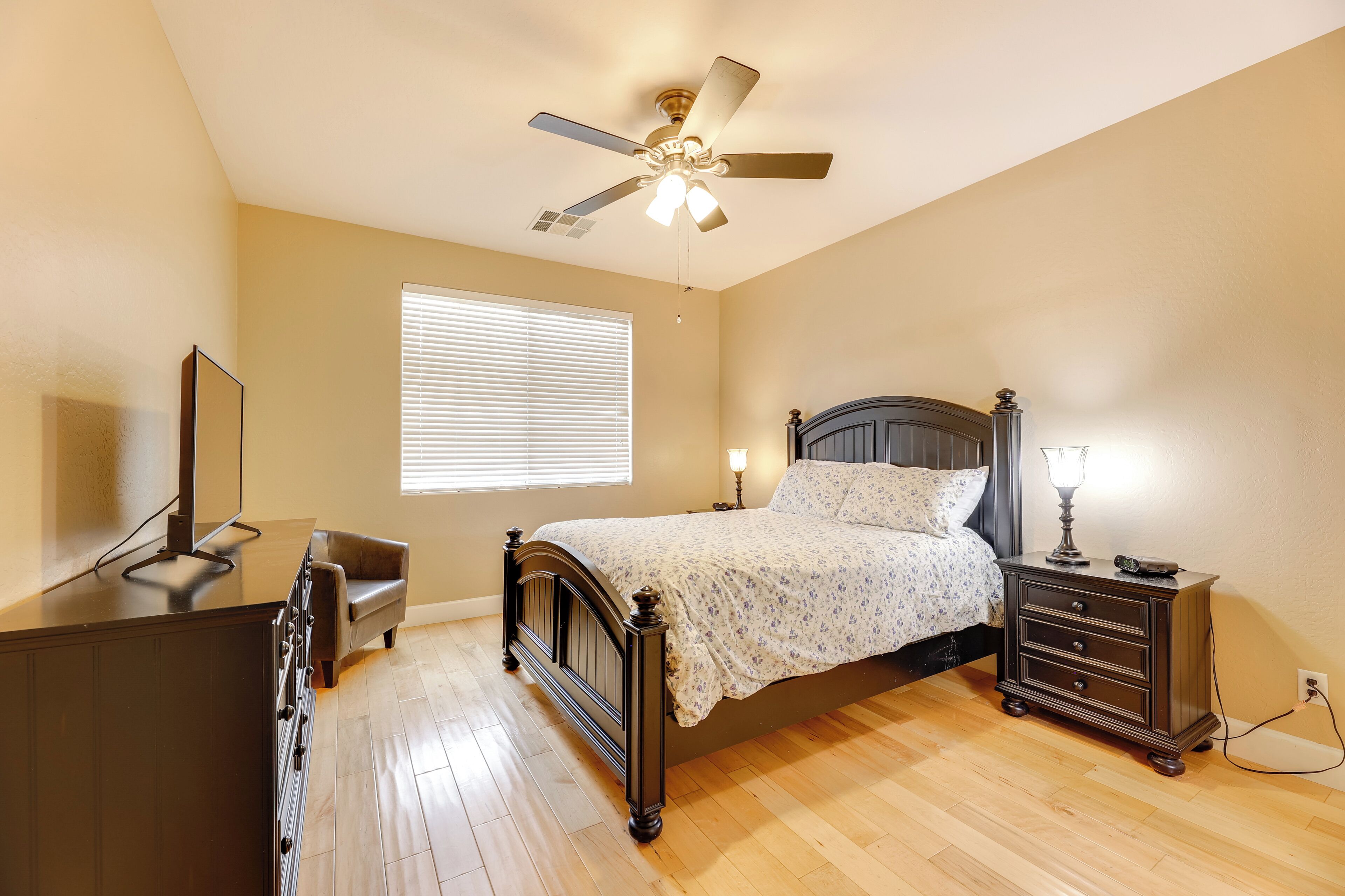 A bedroom with a bed, dresser, vanity, and a ceiling fan.