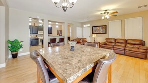 A spacious living room with a large dining table, leather sofa, and a kitchen in the background. - Family Home w/ Community Perks - 8 Mi to Chandler! (Gilbert)