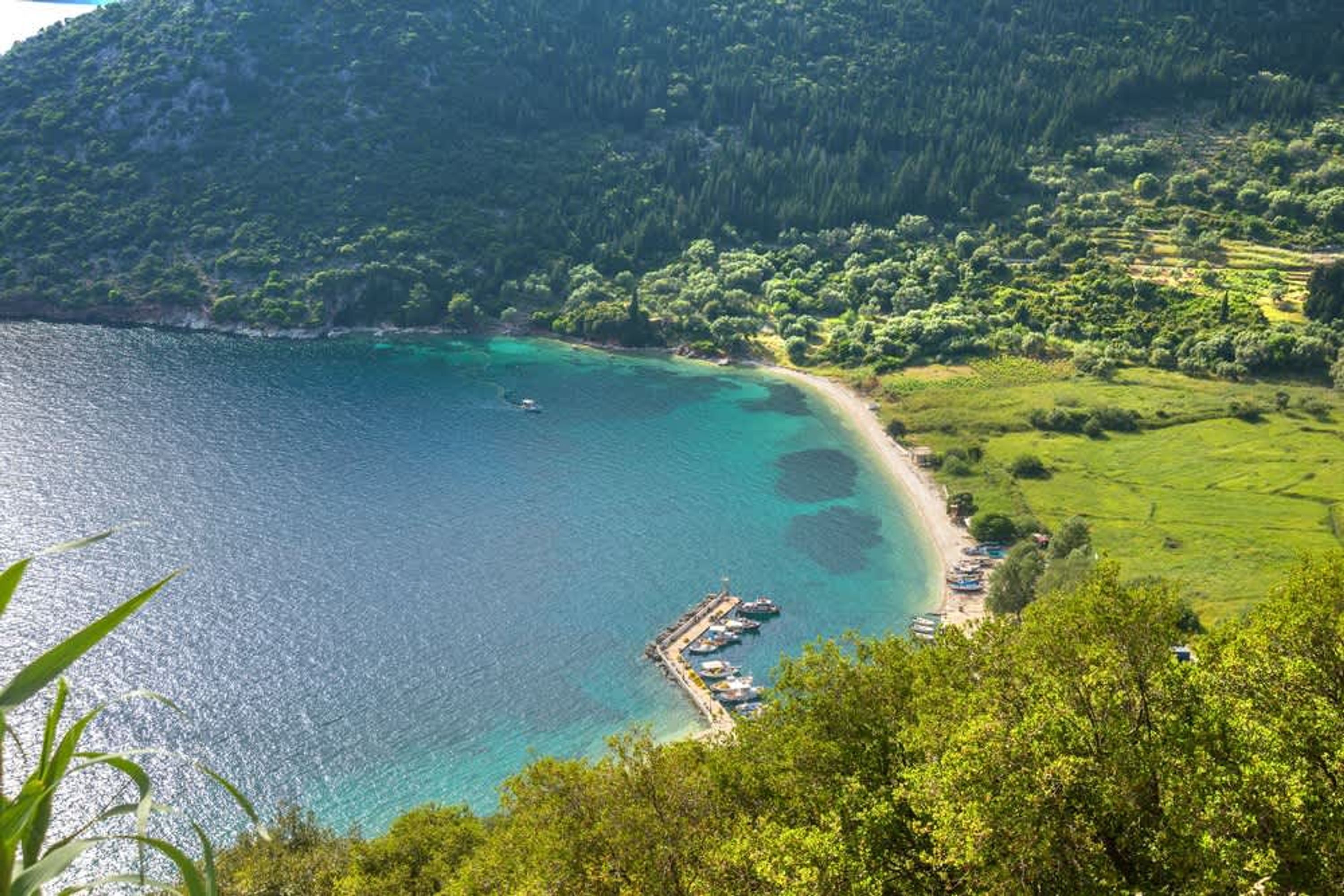 Un paysage côtier avec un quai et des bateaux, entouré d’une végétation luxuriante et d’une mer d’un bleu limpide.