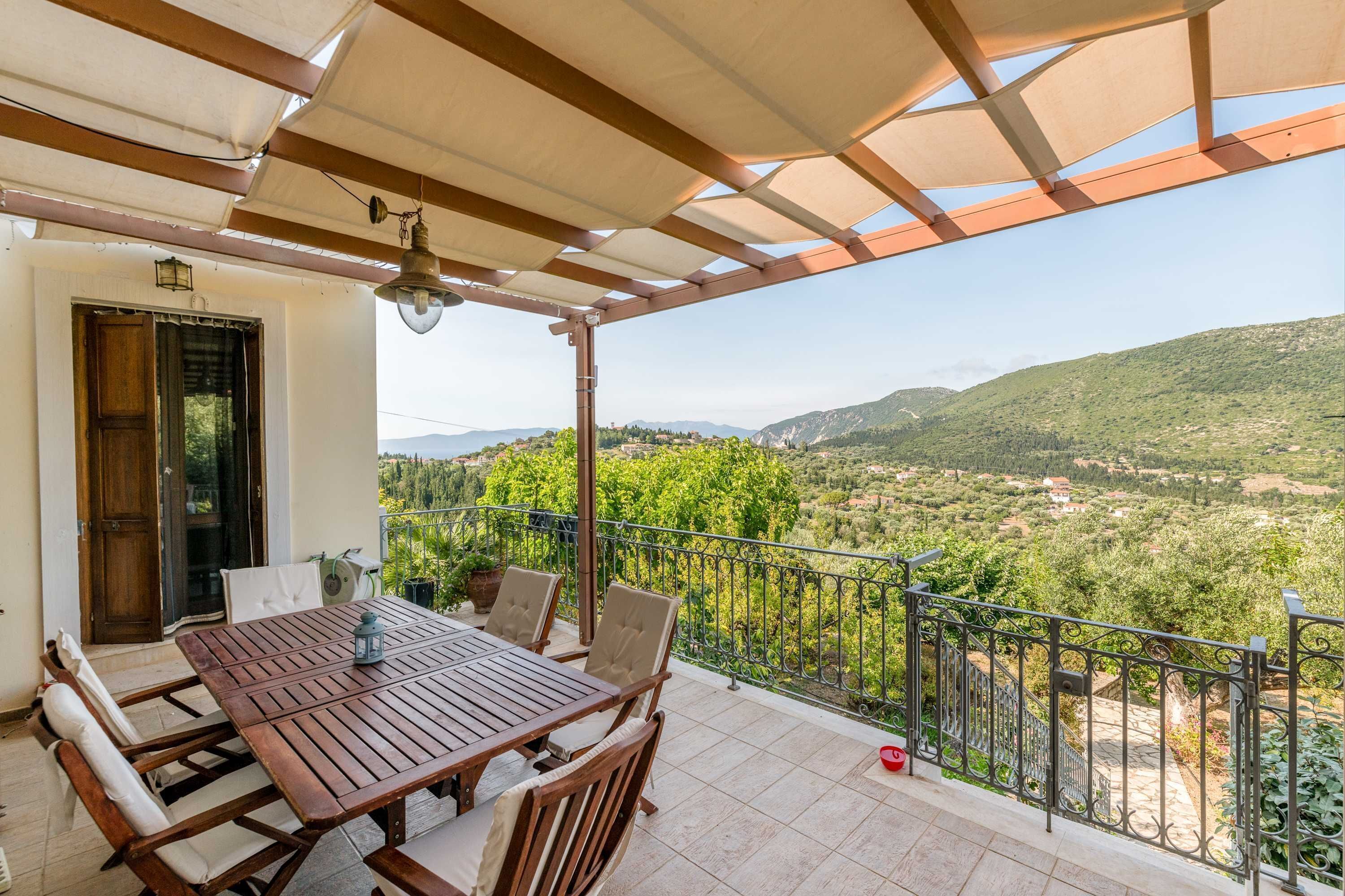 A wooden table and chairs on a balcony with a view of a hilly landscape.