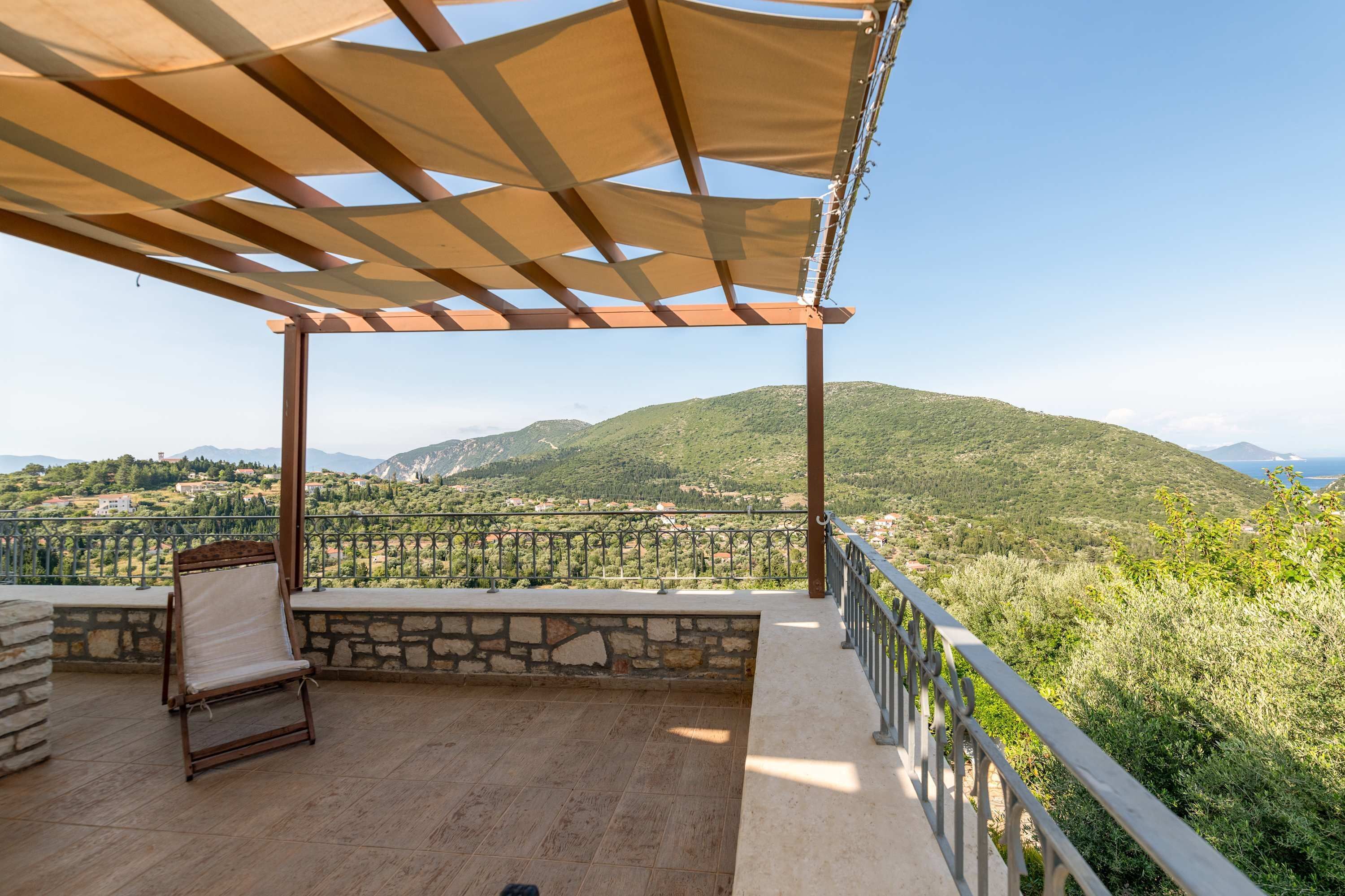 A terrace with a pergola, stone walls, and a view of a hilly landscape.