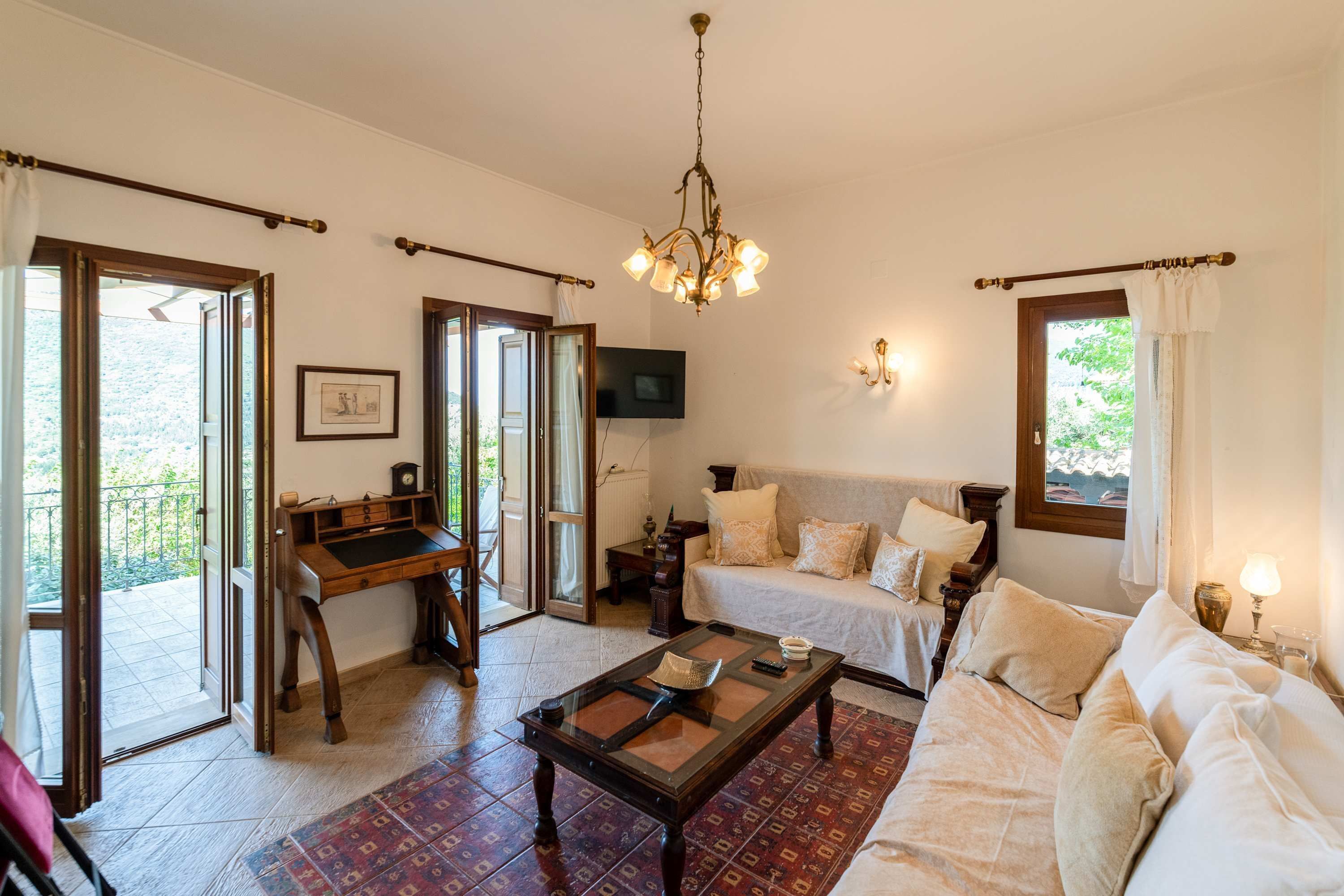 A room with a wooden desk, a sofa, a bed, and a chandelier.
