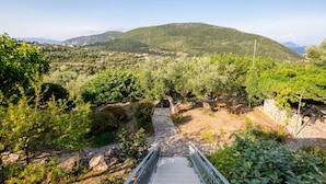 Un escalier en pierre mène à une terrasse d’où l’on peut admirer un paysage montagneux et, au loin, une étendue d’eau.