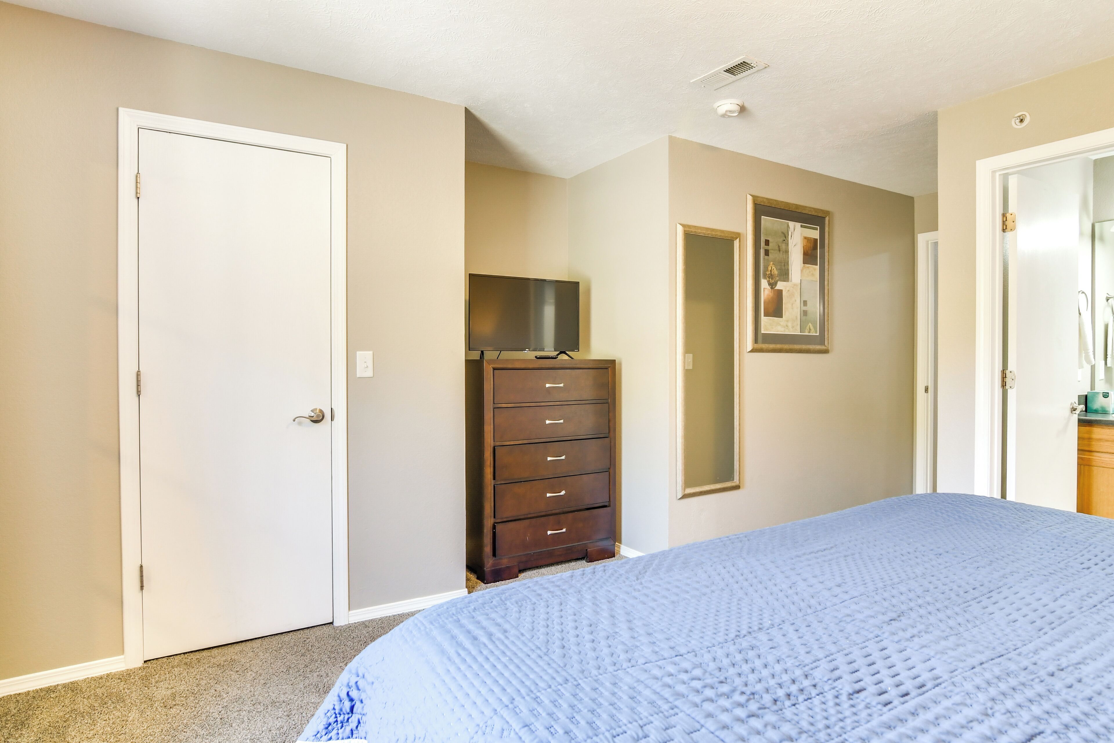 Une chambre à coucher avec un lit, une commode, une télévision et un miroir.