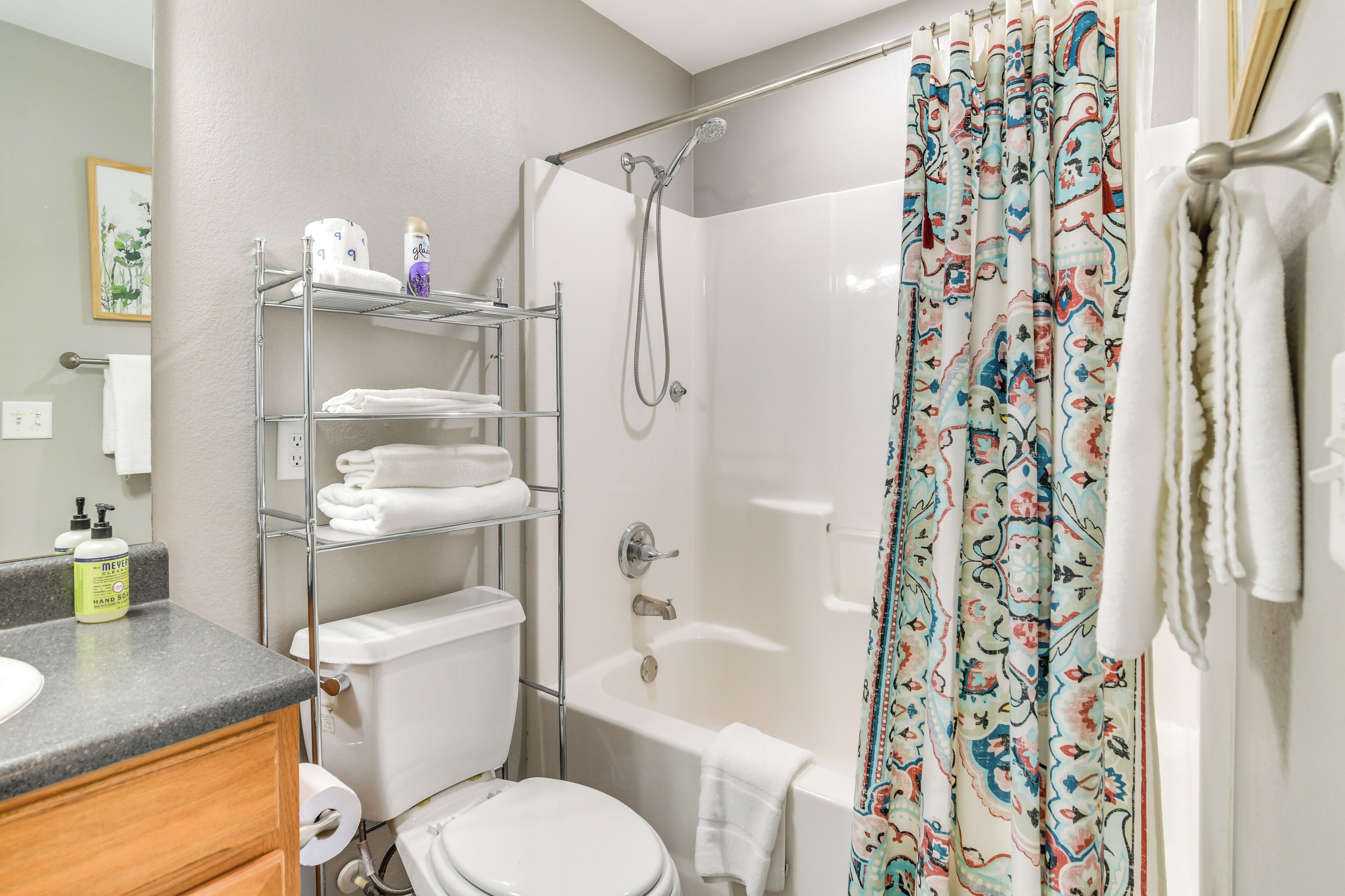 A bathroom with a toilet, sink, shower, and bathtub. There are shelves with towels and toiletries.