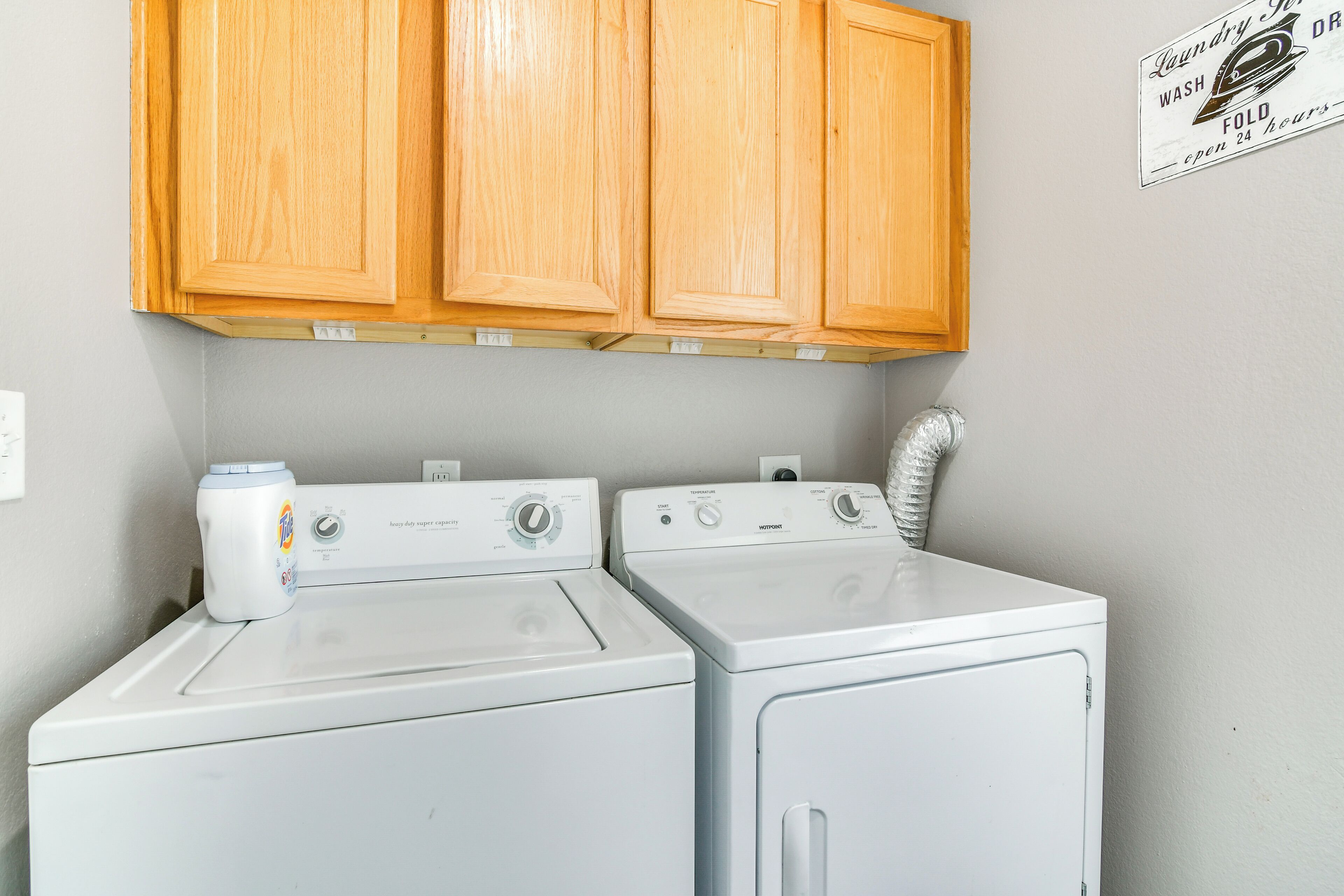 A laundry room with two front-loading washers and dryers, wooden cabinets above, and a sign indicating 24-hour service.