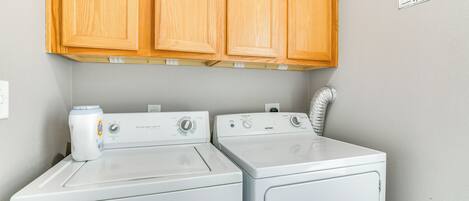 A laundry room with two front-loading washers and dryers, wooden cabinets above, and a sign indicating 24-hour service.