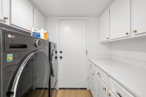 A compact laundry room with an LG washer and dryer, white cabinets, and a door. - Luxe Spacious Home Near Parks Fully Equipped (Riverside)
