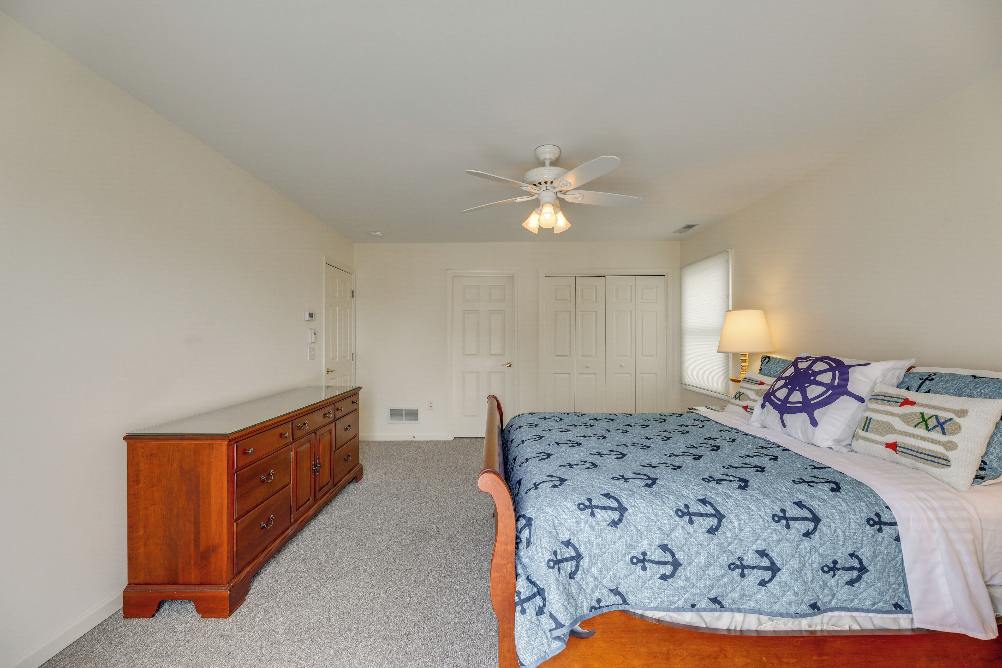 A bedroom with a bed, dresser, ceiling fan, and a door in the background.