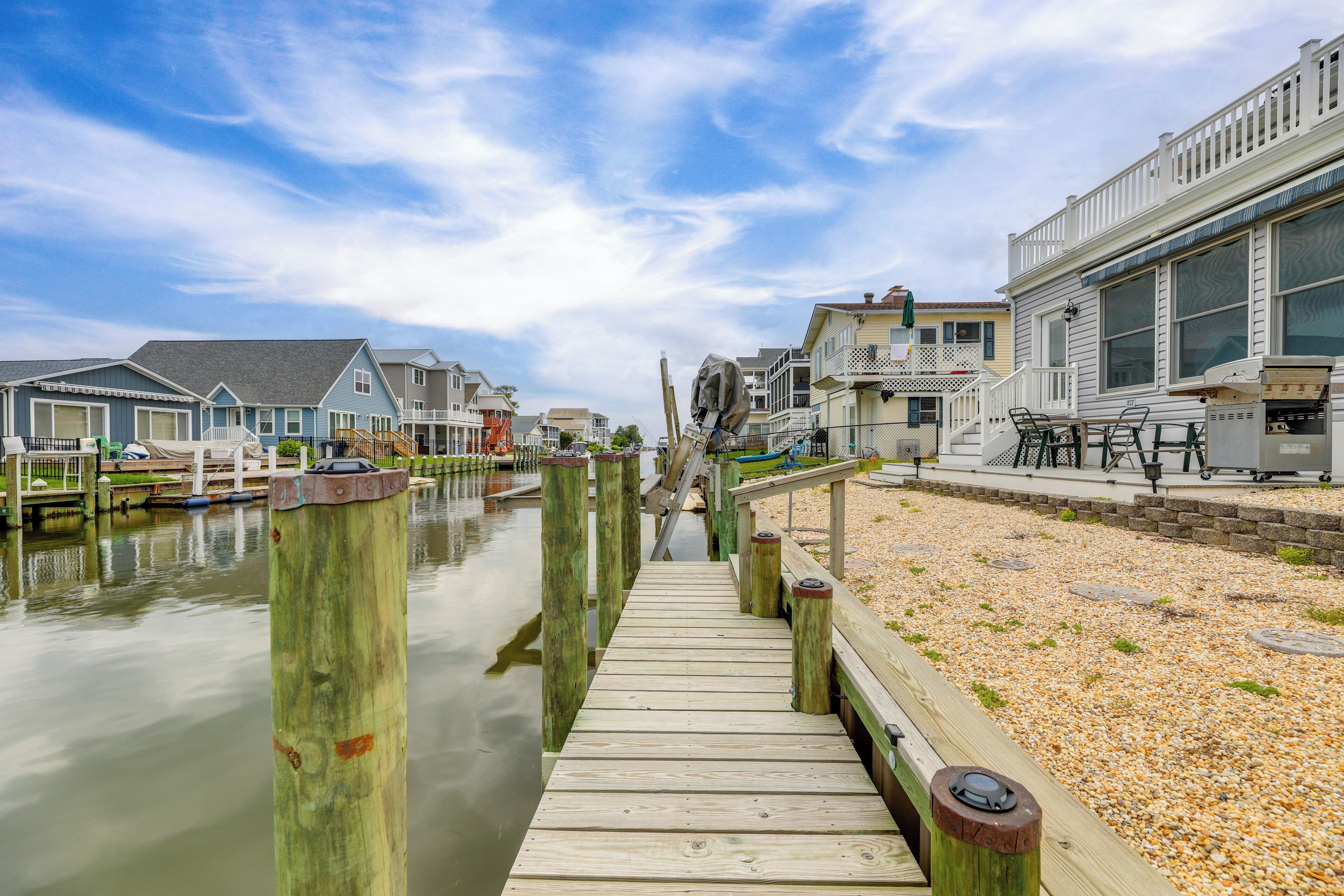 A wooden pier leading to a dock with boats, surrounded by residential buildings with balconies and outdoor seating areas.