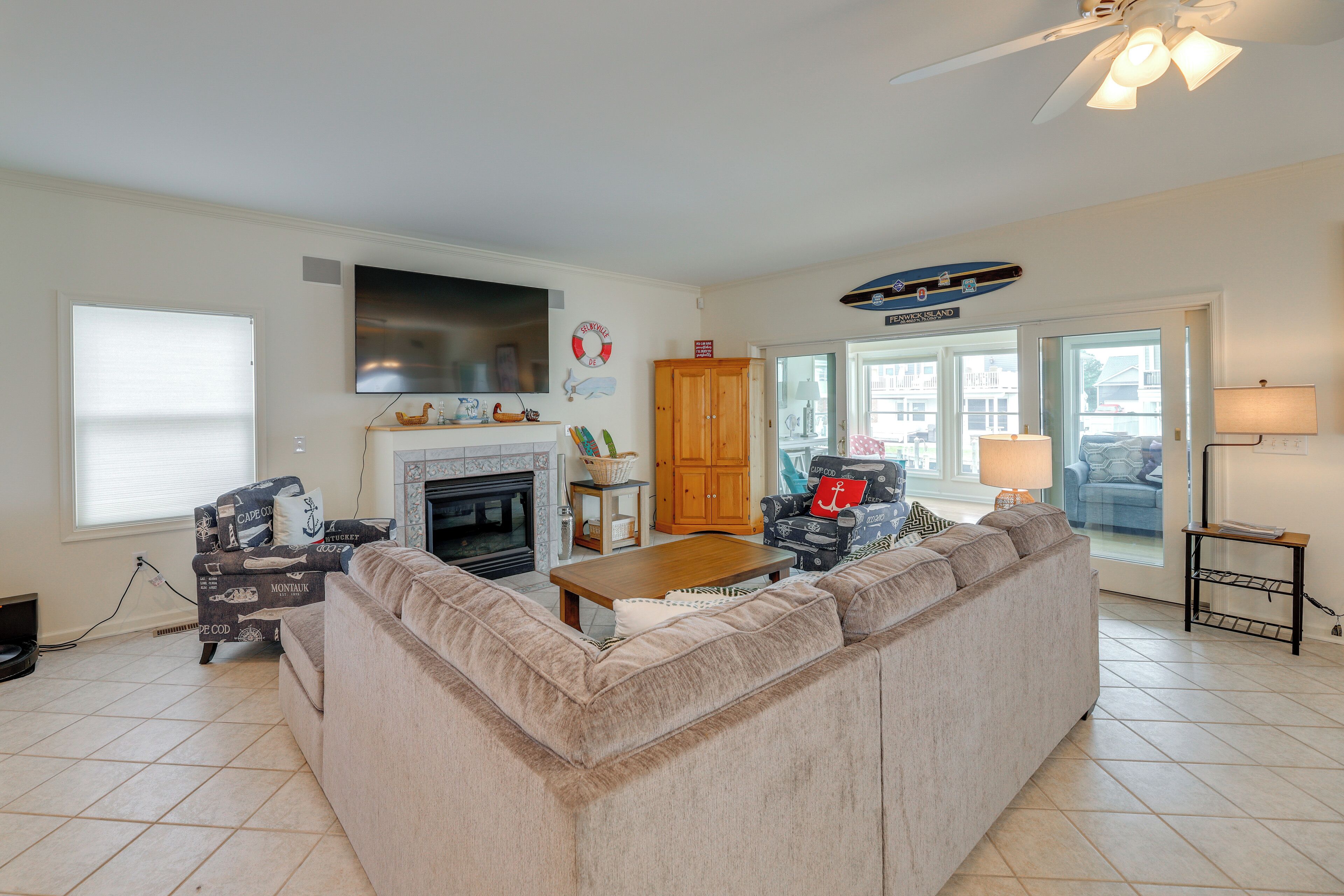 A living room with a fireplace, a large sofa, a television, and a view of the outside.