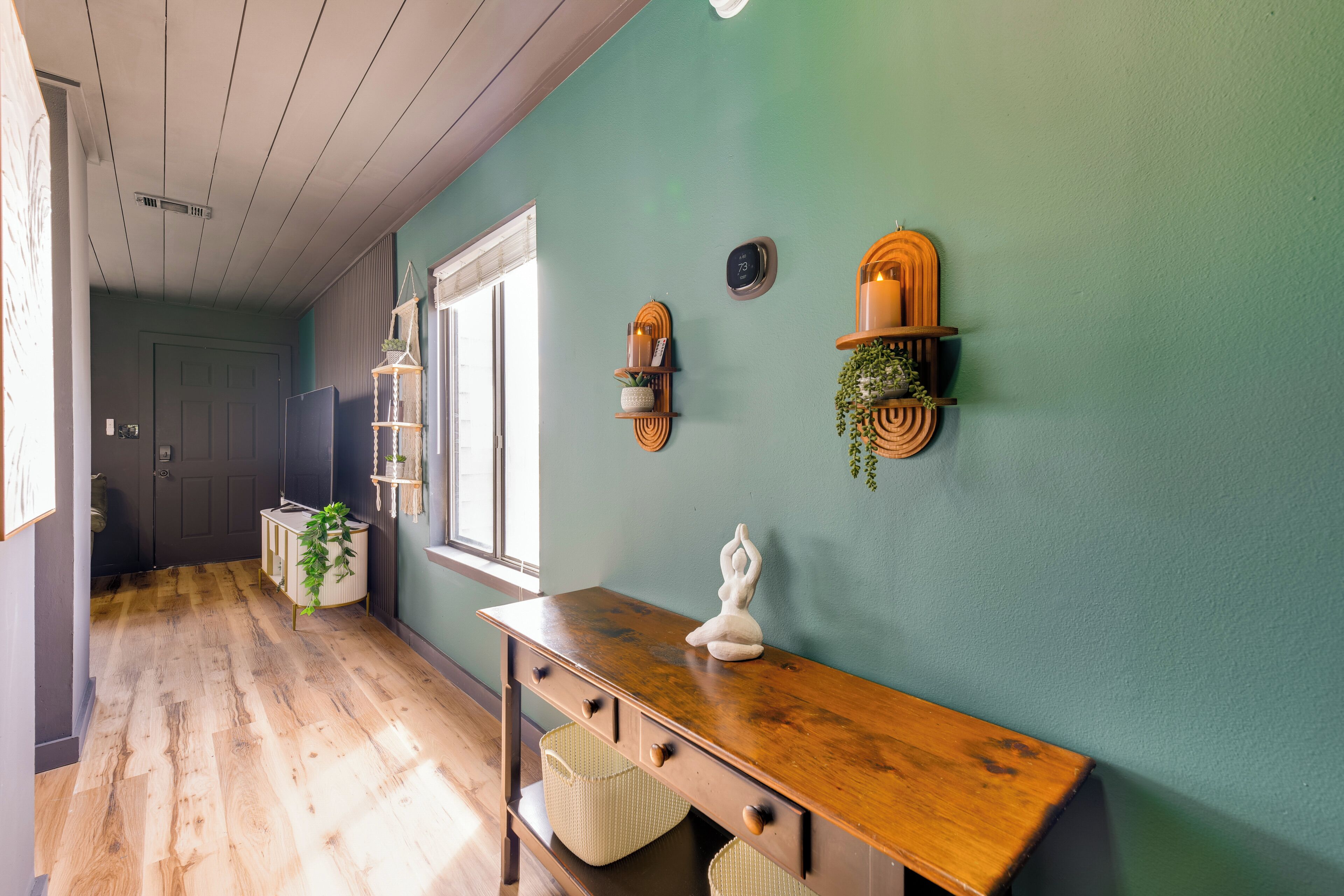 A hallway with a wooden floor, a white console table with baskets, a statue, and wall-mounted shelves with plants.