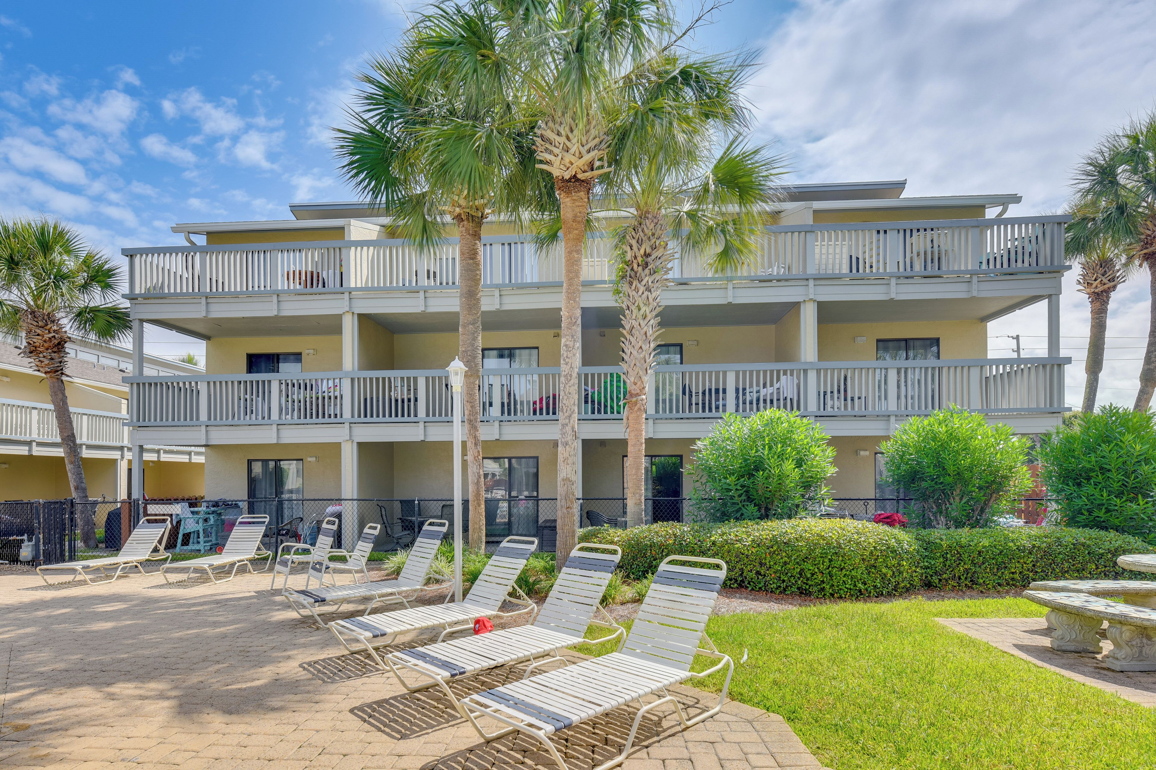 A multi-story hotel with balconies, sun loungers, and palm trees.