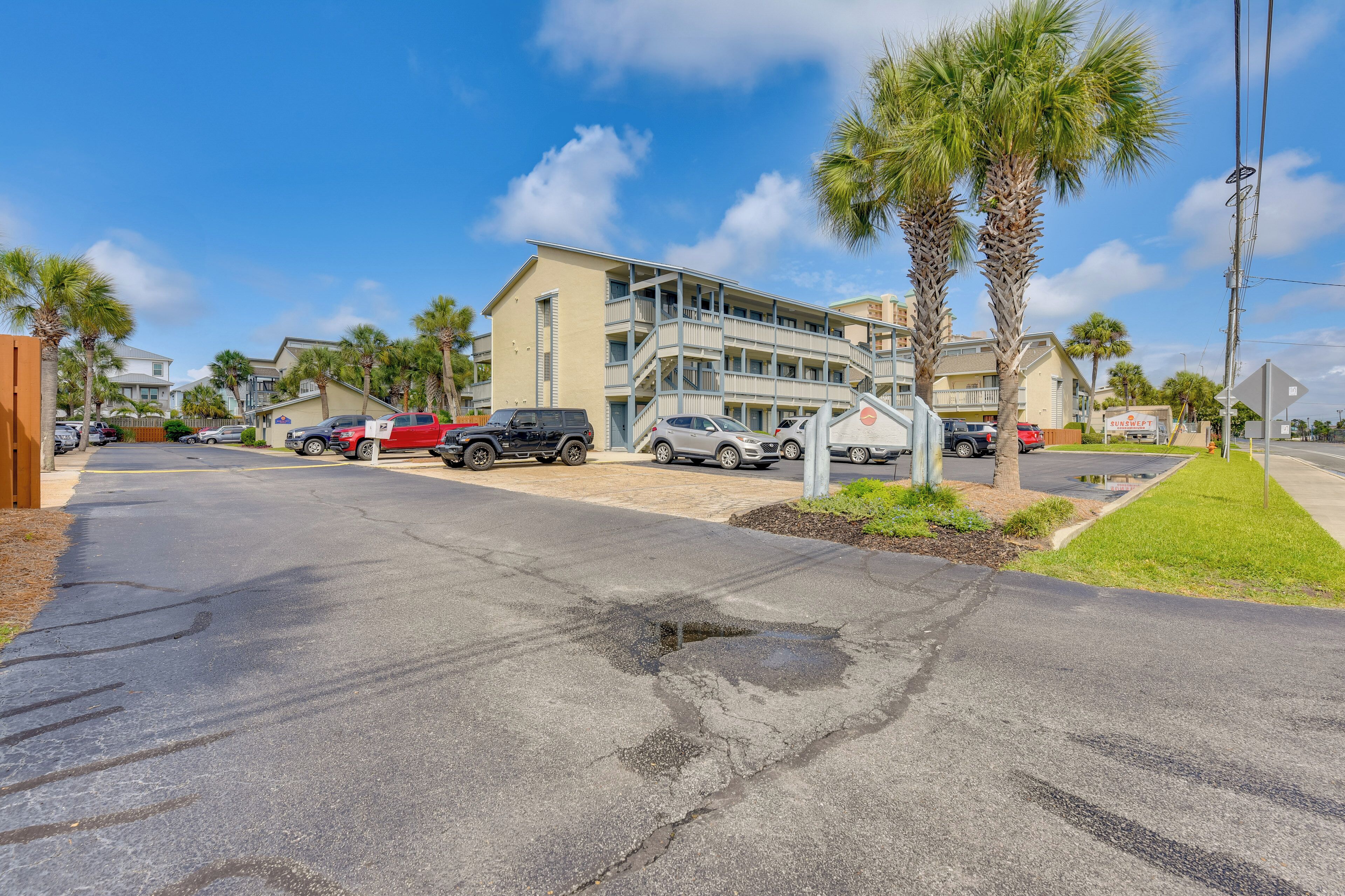 A multi-story hotel with a parking lot, palm trees, and a clear blue sky.
