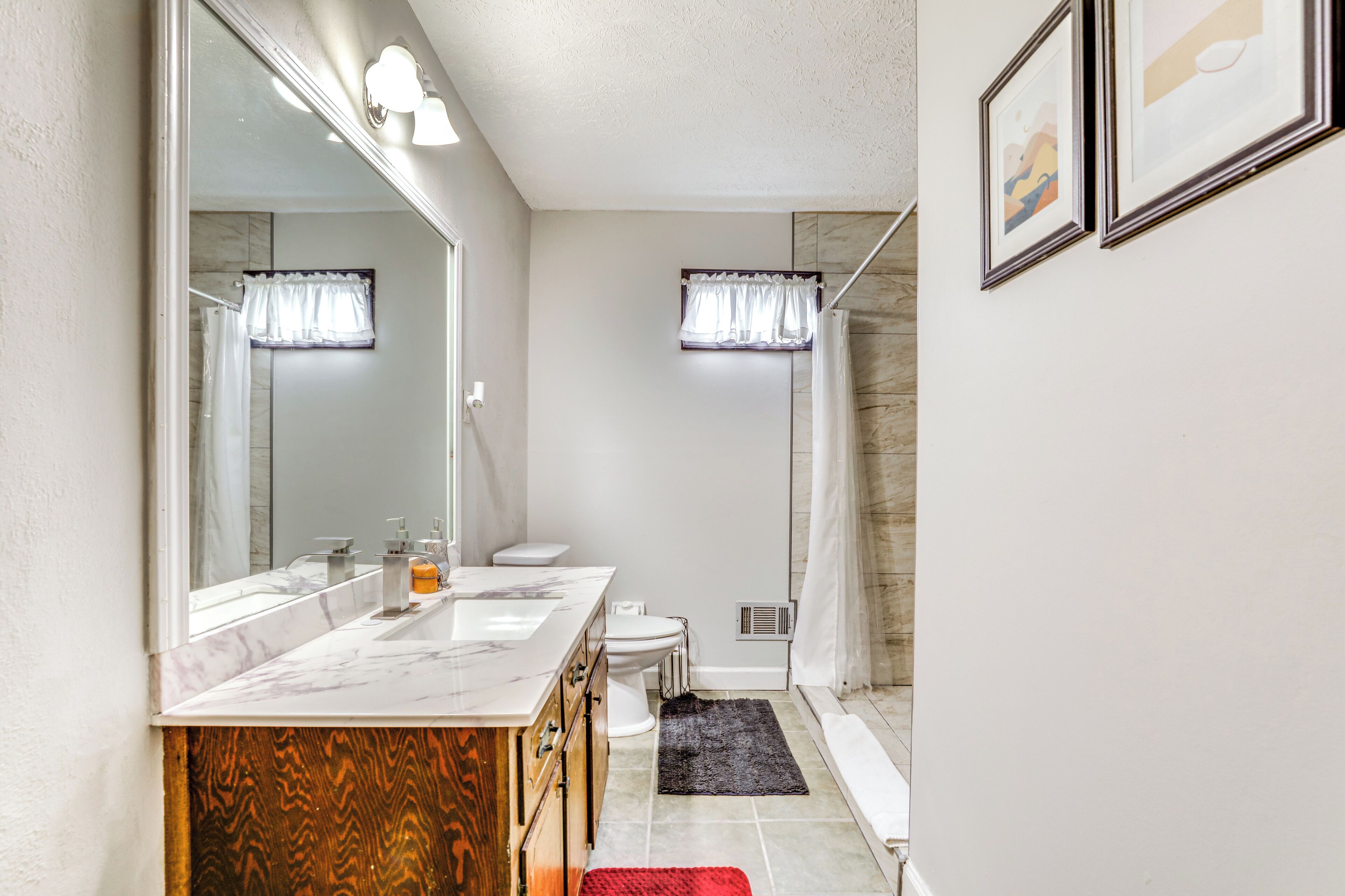 Een moderne badkamer met een marmeren wastafel, een grote spiegel, een douche met glazen deur en een zwart vloerkleed.
