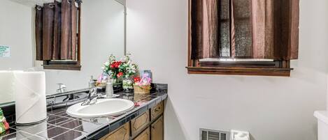 Un baño con lavamanos, espejo, cortinas marrones y una ventana.
