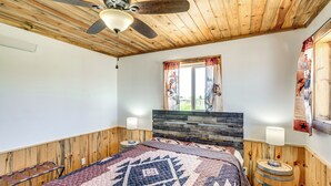 A bedroom with a wooden ceiling, a bed with a patterned quilt, a headboard, a window with curtains, and a wall-mounted lamp. - 2 Mi to Big Hole River: Mtn-view Montana Haven (Twin Bridges)