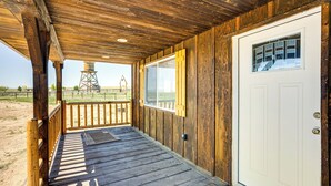 A wooden porch with a white door and a window, leading to a sandy landscape with a water tower in the distance. - 2 Mi to Big Hole River: Mtn-view Montana Haven (Twin Bridges)