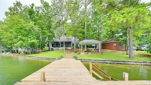 A wooden dock leading to a house with a covered porch, a small brick building, and a pond. - Waterfront Gem on Lake Martin w/ Kayaks & Dock! (Eclectic)