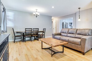 Een moderne woonkamer met een houten salontafel, een leren bank, een eettafel met stoelen en een keuken die door een open deur zichtbaar is.