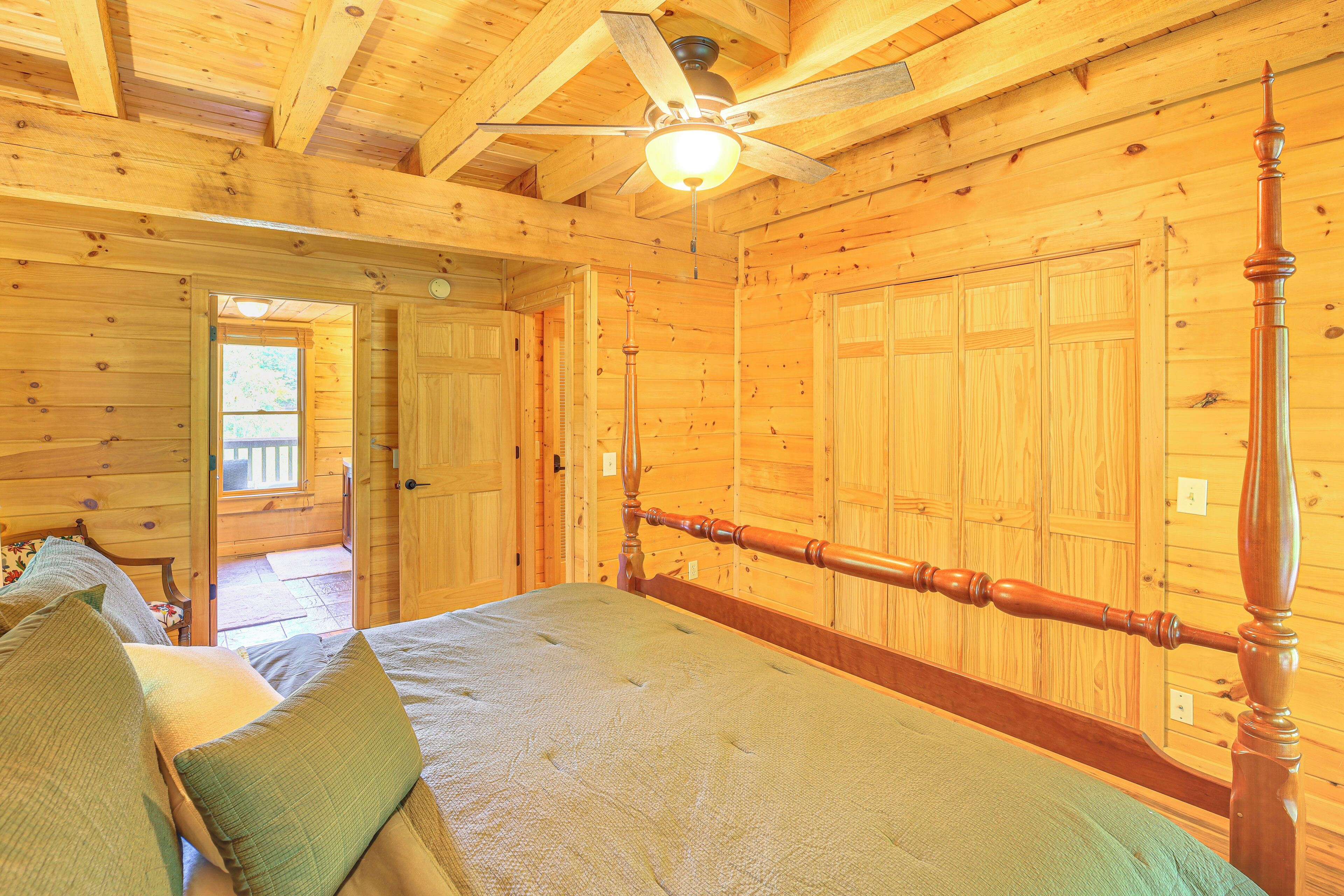 A wooden cabin bedroom with a four-poster bed, a ceiling fan, and wooden walls.
