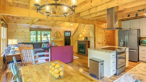 A spacious log cabin interior with a wooden dining table, a sofa, a kitchen area with modern appliances, and a staircase leading to an upper level. - Blue Ridge Mtns Retreat w/ Views, 1 Mi to Parkway! (Hillsville)