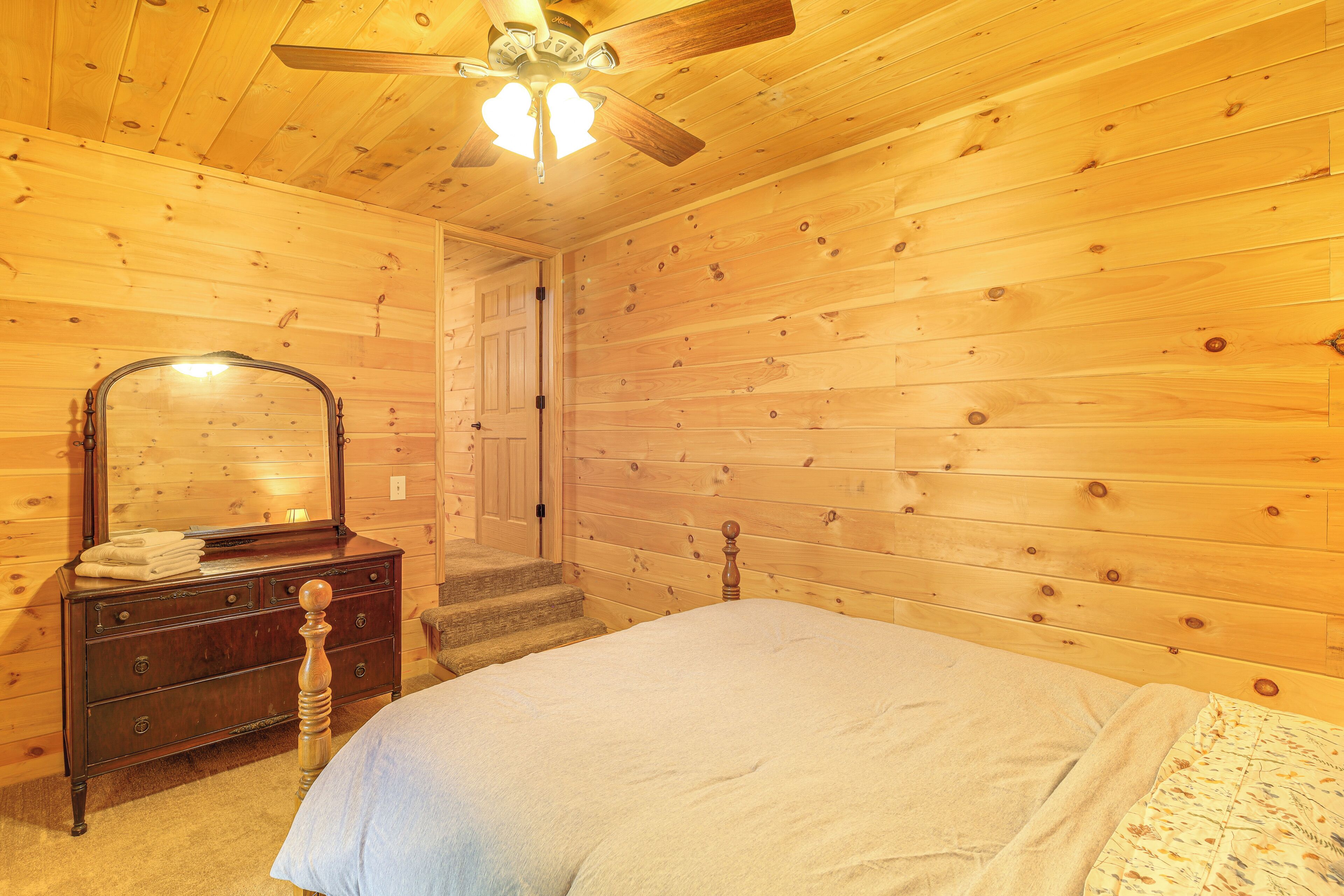 Quarto com painéis de madeira, uma cama, cômoda, espelho e um ventilador de teto.