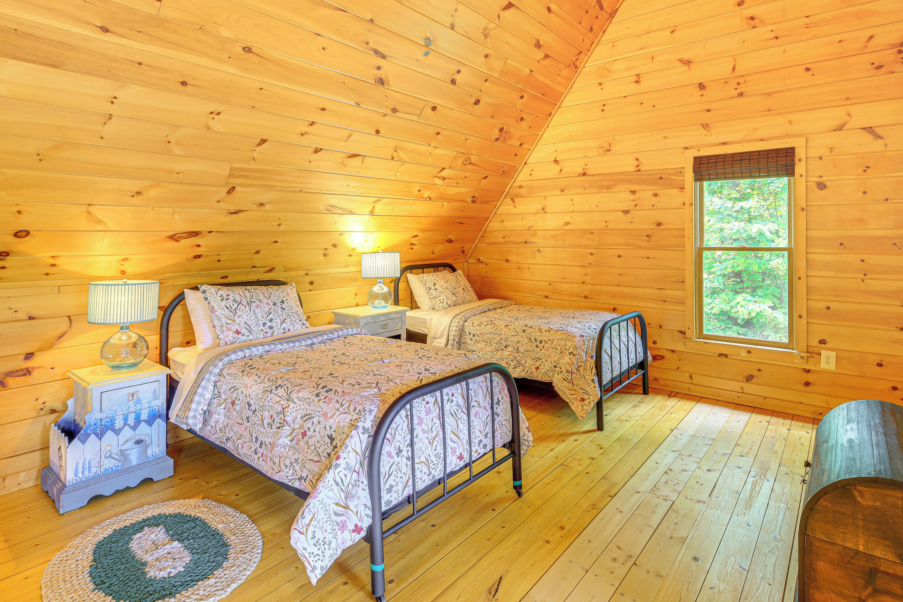 Accogliente camera da letto in una baita di legno, con due letti, un comodino con lampada e una finestra vista verde.