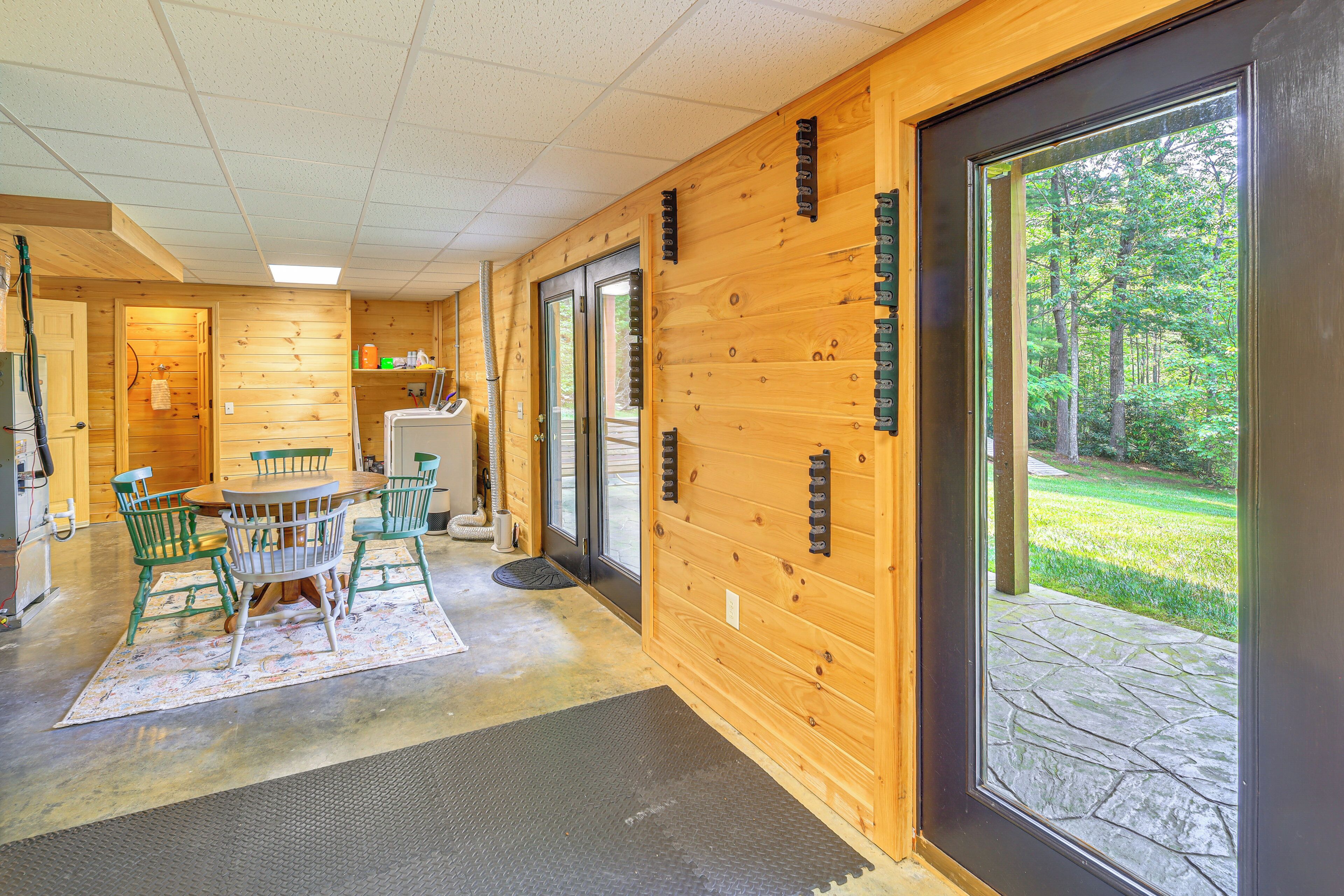Un intérieur en bois avec une table ronde et des chaises, une porte donnant sur l’extérieur et une vue sur un patio en pierre.