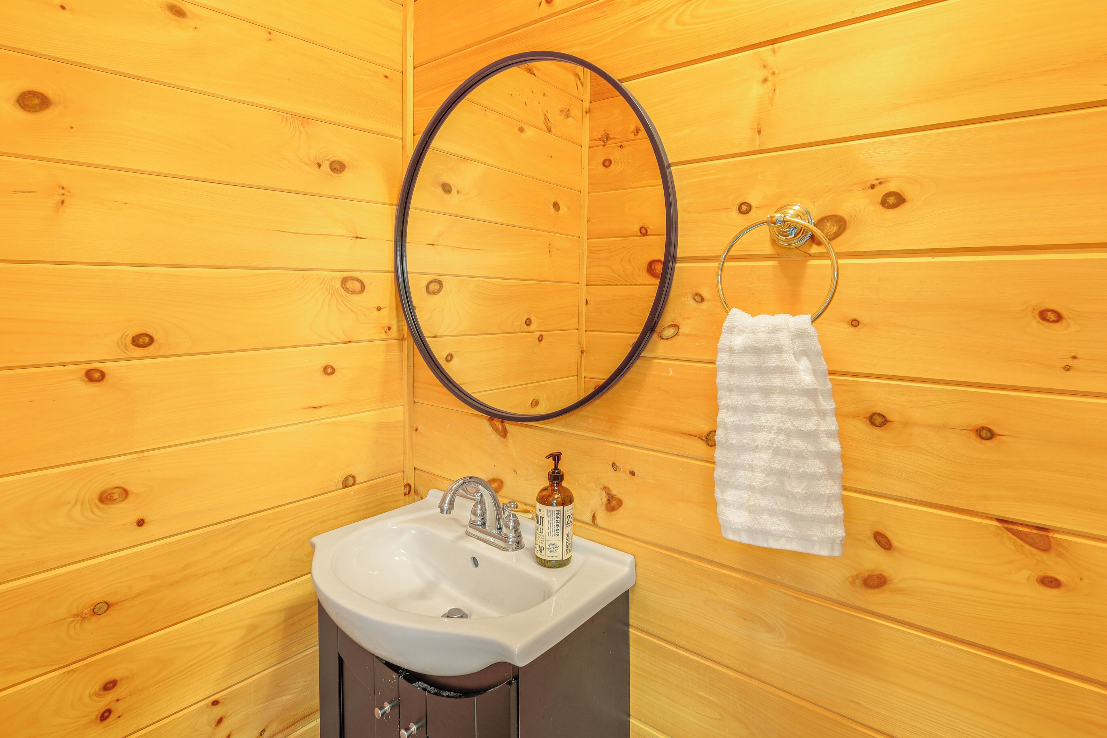Une salle de bain rustique, avec des murs en bois, comprenant un lavabo, un miroir et un porte-serviettes.