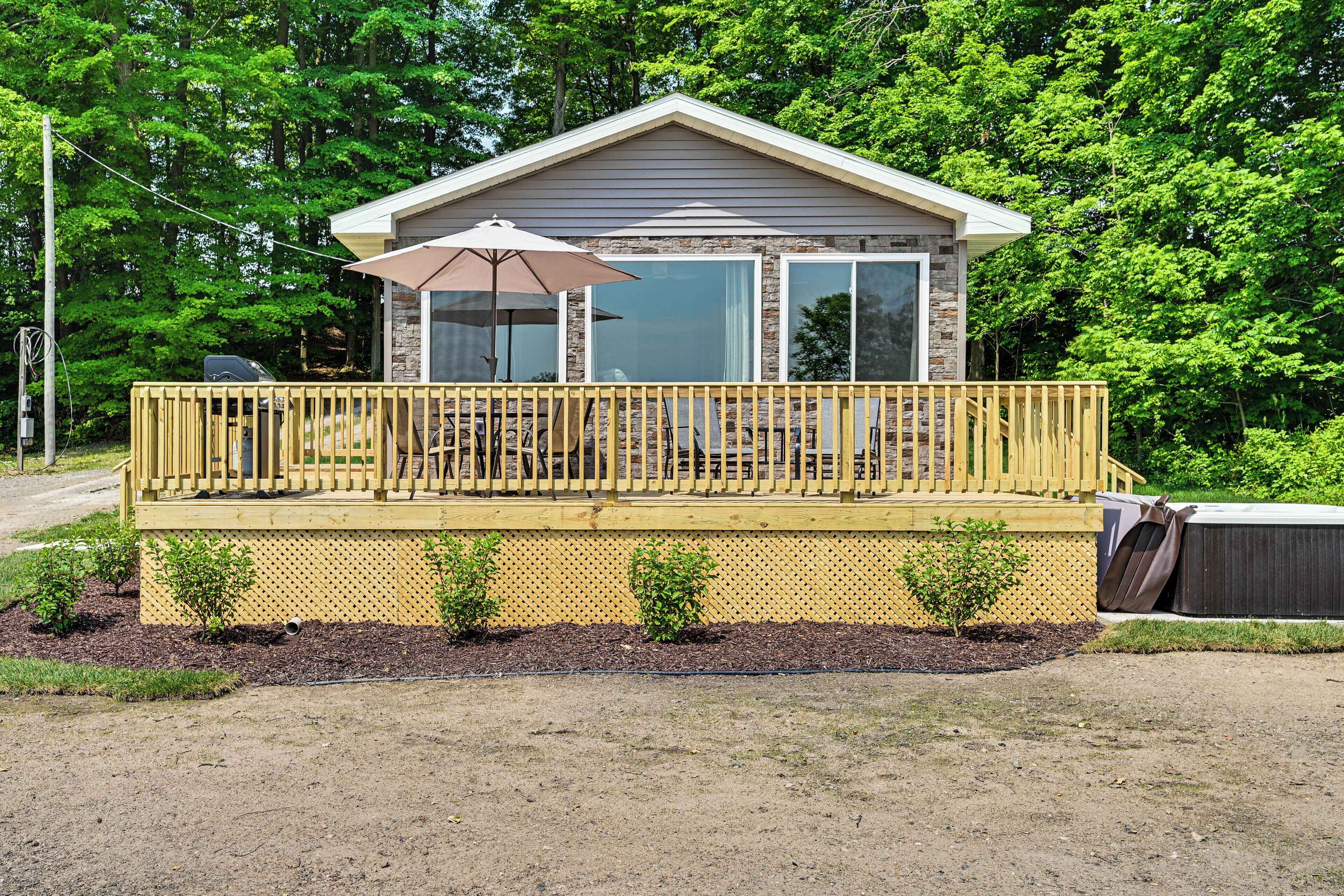 A small, single-story cabin with a deck, a patio umbrella, and a stone facade.