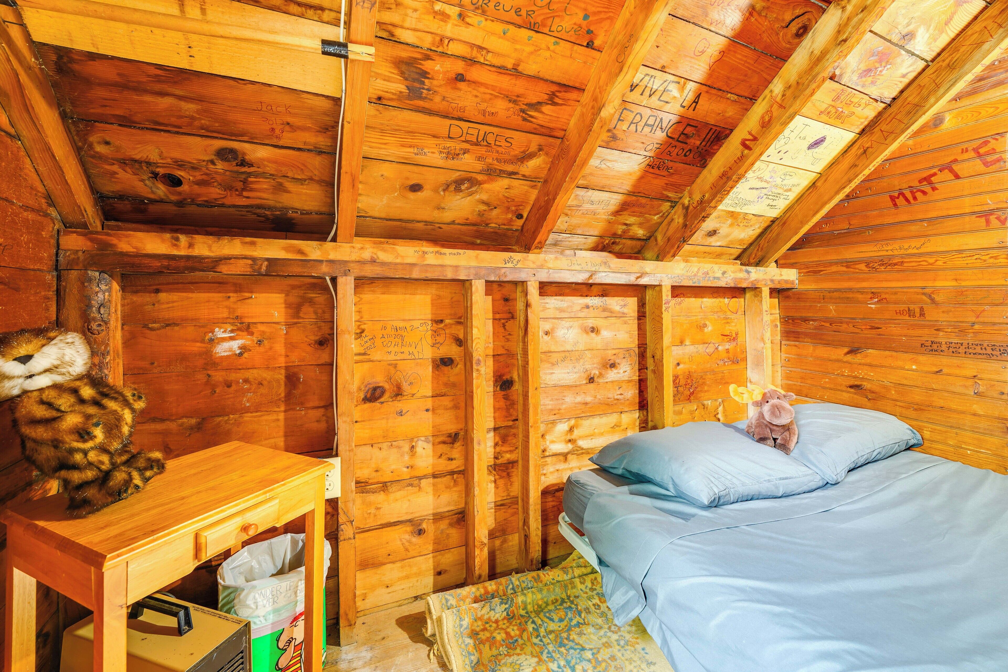 A wooden cabin room with a bed, a small table, and a stuffed animal.