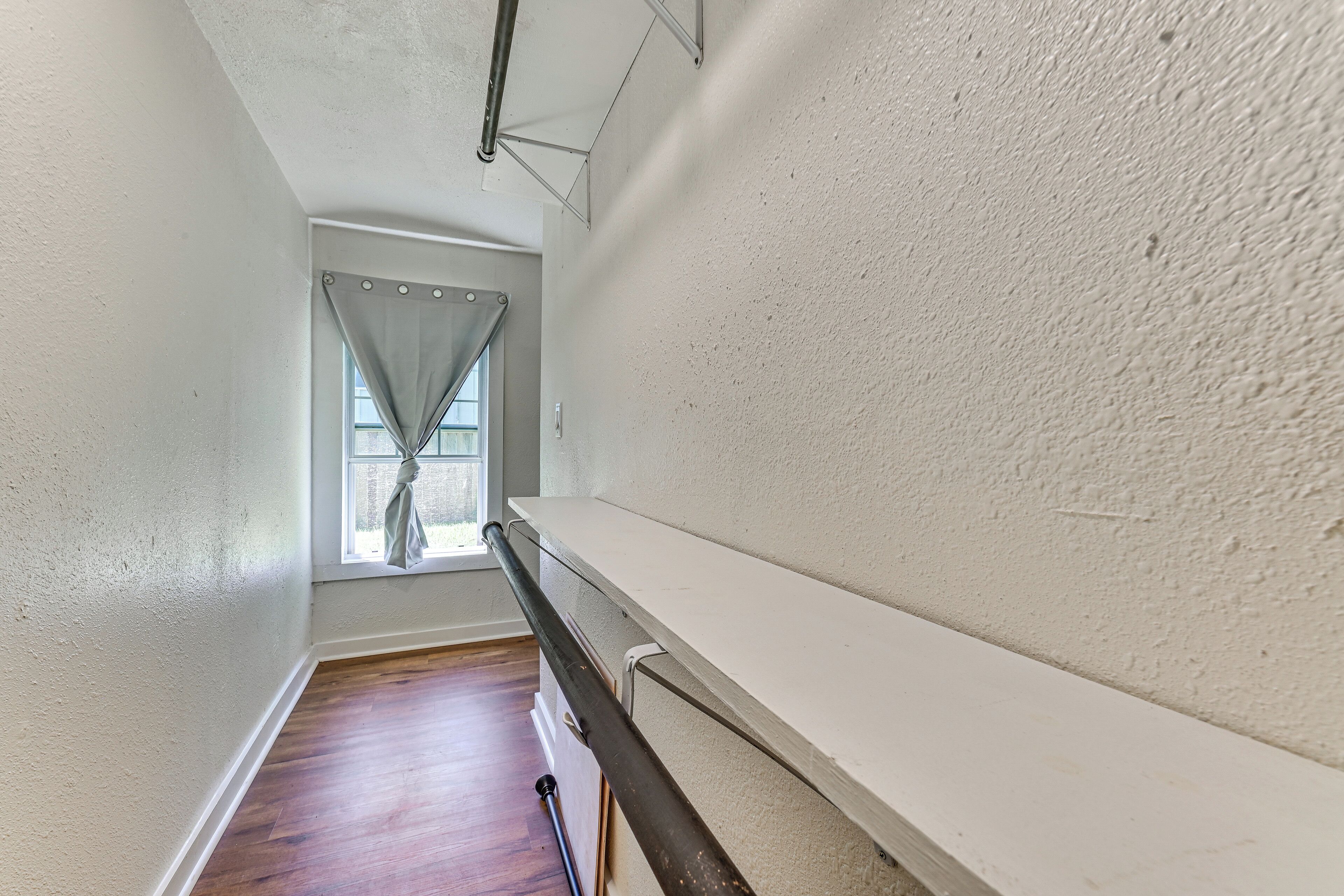 A narrow hallway with wooden flooring, white walls, and a window with curtains.