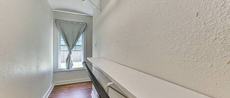 A narrow hallway with wooden flooring, white walls, and a window with curtains.