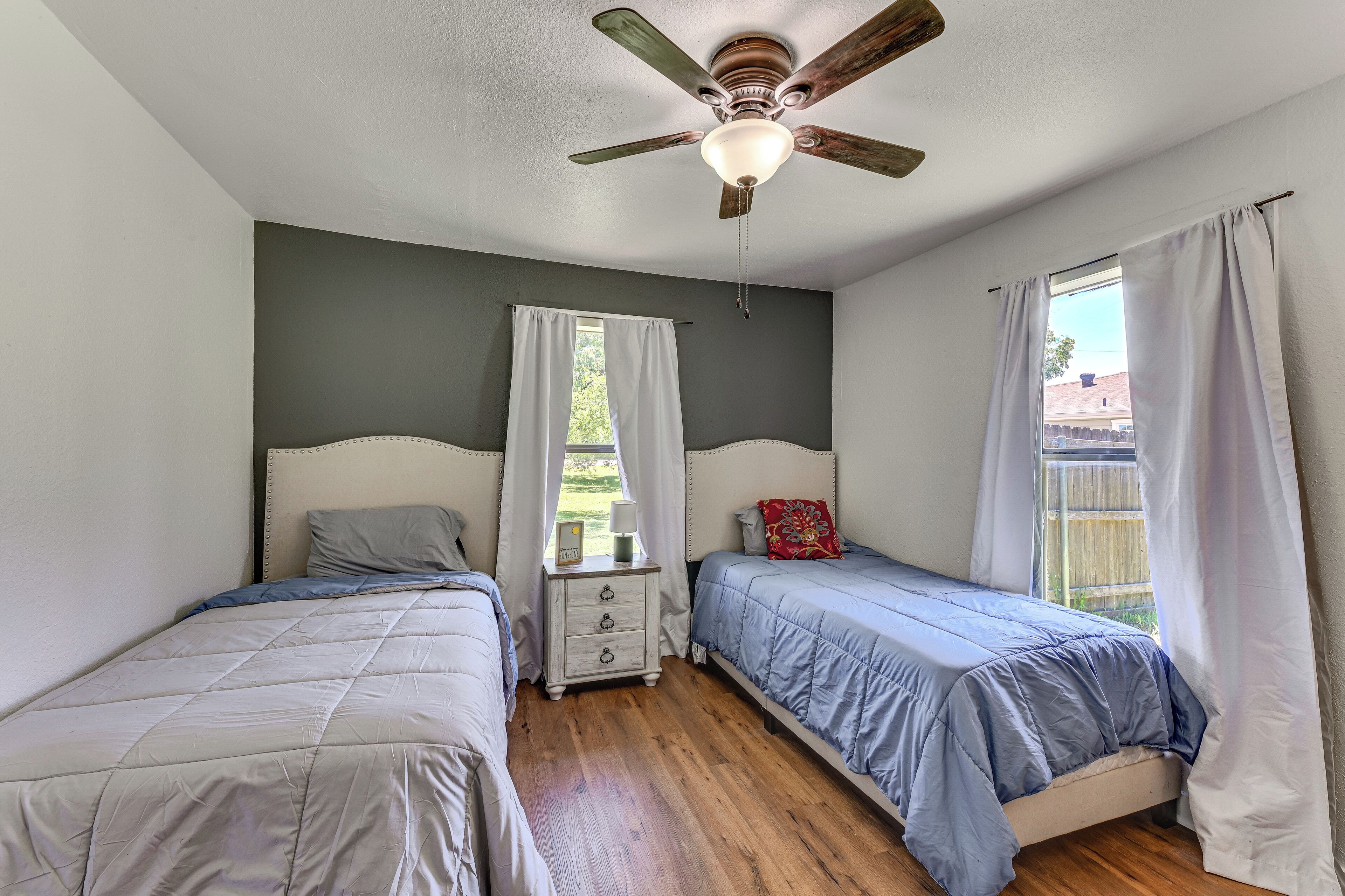 A bedroom with two beds, a ceiling fan, and a window with curtains.
